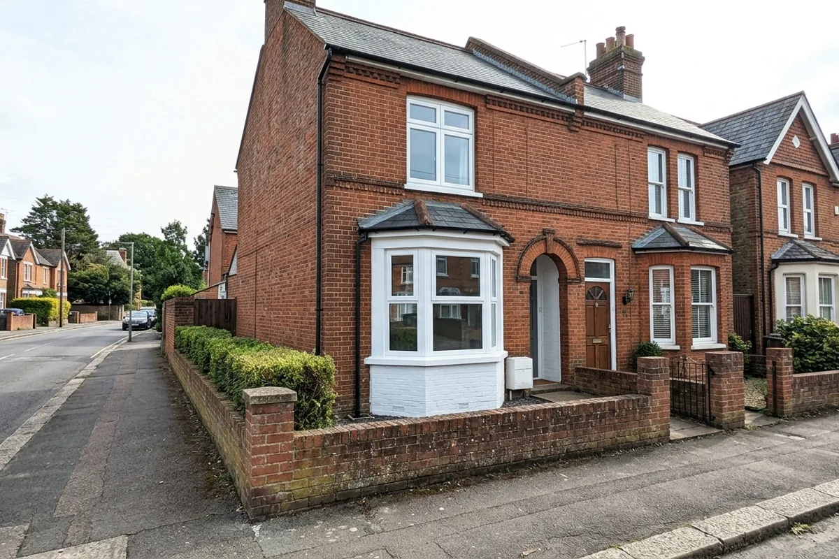 An Edwardian red-brick semi-detached house in Redhill with a new white uPVC three-unit canted bay on a solid painted brick base and a low garden wall, nothing in front of the bay